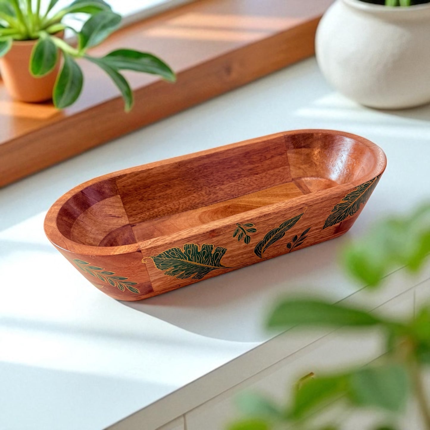 Wooden bowl with leaf patterns on a light surface, surrounded by potted plants.
